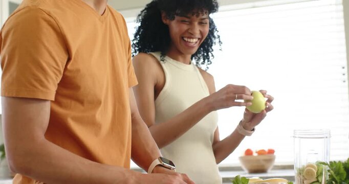 Making smoothie, couple chopping and blending at counter with blender and woman offering apple bite