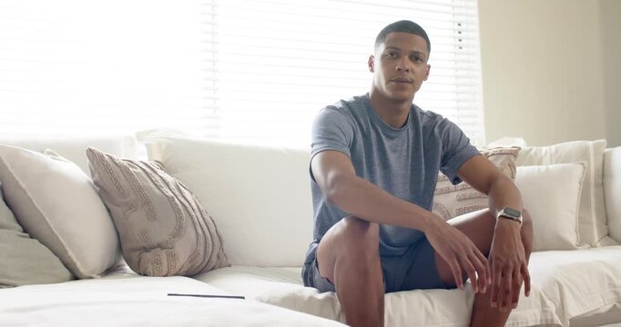 African American man entering living room settling onto sofa then examining smartphone and smiling