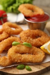 Deep fried squid rings with lemon slice, basil and ketchup on wooden table, closeup