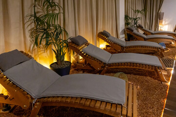 Modern spa lounge with row of stylish beige wooden recliners,. Relaxing area with contemporary design and dim lights, silent tranquil atmosphere. pieces of amber on floor, stone therapy