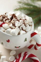 Tasty cocoa with marshmallows, candy canes and Christmas decor on light table, closeup