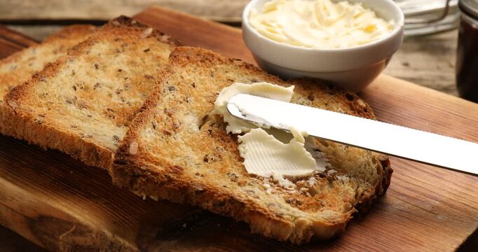 Woman putting butter onto slice of toasted bread on wooden table, closeup