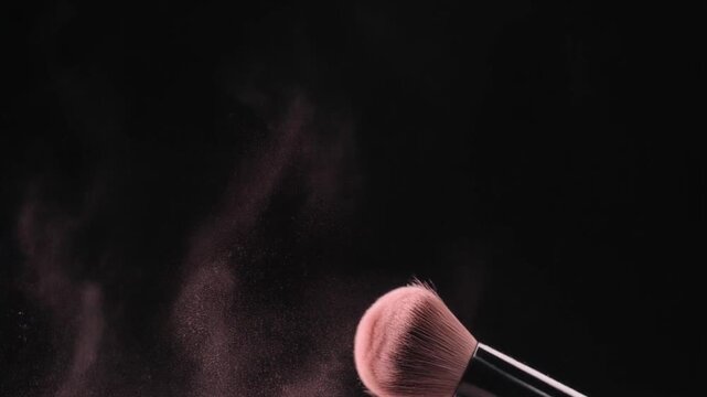 Closeup of a makeup brush dispersing pink powder against a black background. 4k Footage Video