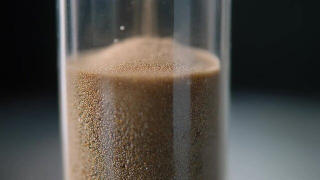 Detailed macro view of sand grains falling in a classic hourglass timer.