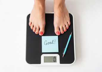 Woman bare feet with red toenails on a digital bathroom scale with a goal note