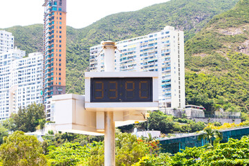 Digital Signs symbol LED electric Thermometer marking show red number 33 degrees celsius. City buildings are nestled in mountain range with sky and white clouds background. Air temperature.