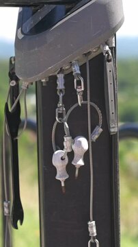 Verti al screen closeup keys and helmet hanging on post in sunlit park, metal keyring with small keys and chain, shallow depth of field, warm summer greenery background, gentle breeze