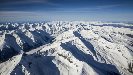Aerial view of snow-covered mountain range under a clear blue sky.