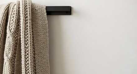 Cozy chunky knit wool scarf hanging on a black wall hook against a light minimalist wall for winter fashion concept and home comfort with copy space