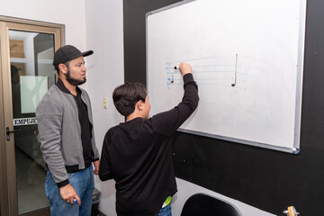 Student writing musical symbols on the board while the teacher explains rhythm patterns in a drum and drums class. Music theory, notation learning, structured practice