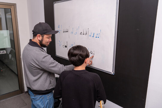 Student practices rhythm writing on the board while the teacher offers corrections in a music class. Music notation, solfege study, structured rhythm education
