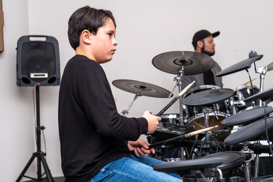 Young drum student focused on the teacher&rsquo;s movements while they play together at the drum kit. Private lesson centered on rhythm practice, percussion technique, and musical development