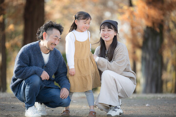 秋の公園で遊ぶ家族 紅葉の森で笑顔の親子の記念撮影　お出かけやレジャーのほのぼの思い出のイメージ