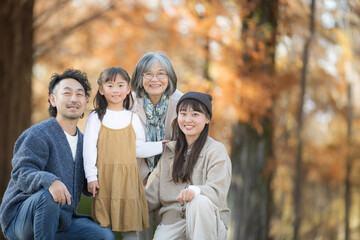 秋の家族写真・紅葉の森で笑顔の三世代家族ポートレート・親子と祖母の記念撮影　カメラ目線思い出のイメージ　