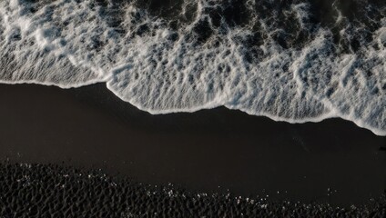 Fototapeta premium Aerial view of black sand beach with foamy ocean waves.