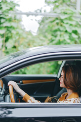 A woman sits in a car, hands on the steering wheel, in profile as she drives, framed by the sleek...
