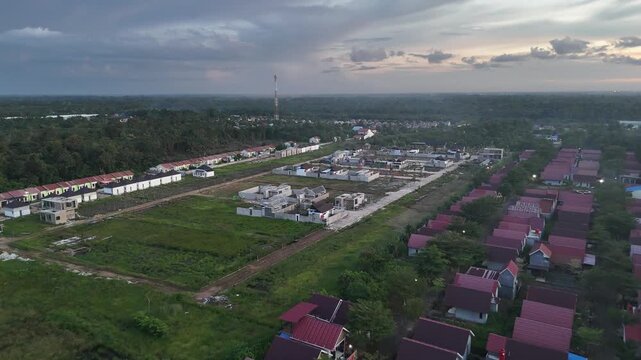 Aerial footage from a drone capturing the developing residential area, with red-roofed houses, undeveloped vacant land, and mature trees. 