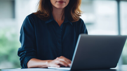 Modern office woman typing on laptop, business professional at work in bright space with calm focus and clean desk setup