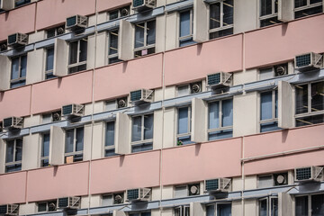 A multi-story building with alternating pink and beige panels, densely packed with air conditioners and window blinds.