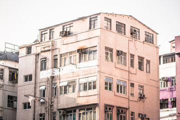 A faded pink residential building with visible pipes, air conditioners, and laundry, reflecting everyday urban life.