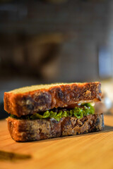 Close-up of a rustic artisan sandwich made with crusty toasted bread and fresh green lettuce on a wooden board. Warm, natural light and shallow depth of field create a gourmet, café-style look.