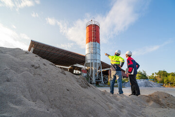 Two engineers inspect aggregate piles and a concrete batching plant at sunset, focusing on material management and small business operations.