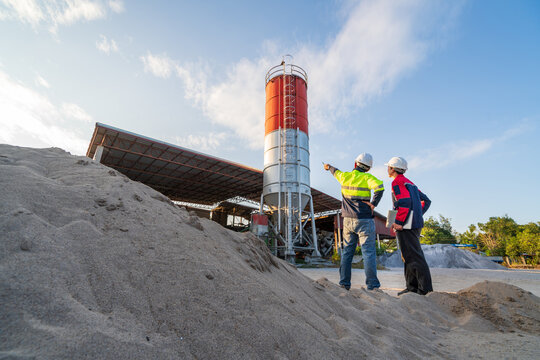 Two engineers inspect aggregate piles and a concrete batching plant at sunset, focusing on material management and small business operations.