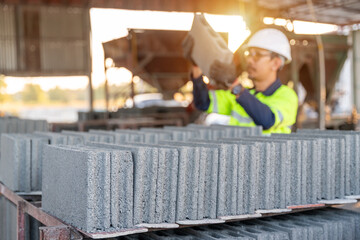 A construction manager carefully lifts a concrete cinder block for inspection, checking the product quality at a small manufacturing plant.