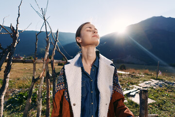 Naklejka premium woman outdoors mountains sunlight nature portrait rural jacket traveler relaxation, portrait of a relaxed young woman in a denim shirt and warm jacket breathing fresh mountain air
