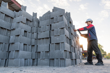 A construction manager inspects a high stack of fresh concrete cinder blocks, focusing on inventory and quality control at a small manufacturing plant.
