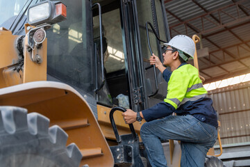 A construction manager in a safety vest climbs into the cab of a wheel loader, preparing to oversee heavy equipment operation at the job site.