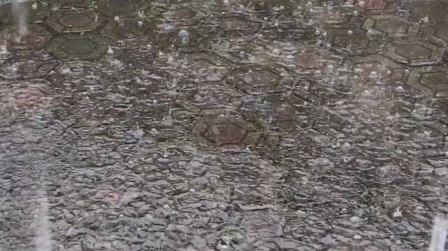 Heavy rain falling on hexagon stone pavement texture. Rain splashing on wet patterned paving block surface. Storm rain drops hitting urban stone walkway background