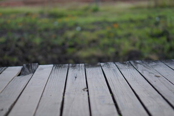 Horizontal gray weathered wooden planks surface with blurred green grass and earth background,...