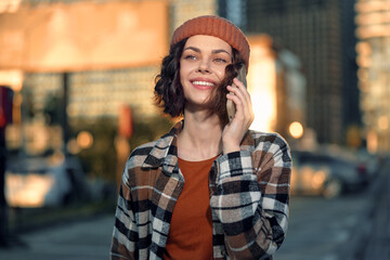 woman on phone with smile in urban street, candid lifestyle portrait at golden hour glow; beanie...