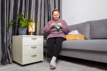 Adult Woman Knitting Yarn and Creating Handmade Items While Relaxing on a Sofa in the Comfort of Her Home
