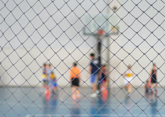 blur basketball court by rope mesh net fence focus with many youth children or kid learning training shooting ball to playing basketball with coach and basketball hoop in school gym for sport exercise