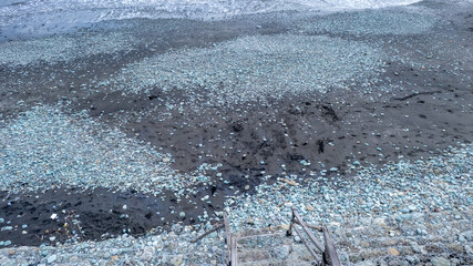 High-angle shot of weathered wooden stairs descending towards a beach covered in dark sand and scattered blue-gray pebbles near the ocean's edge
