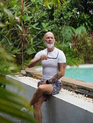 A man is comfortably sitting near a swimming pool in tropical area