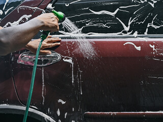 Photo of a man wearing a t-shirt washing or cleaning his car alone. Washing the car with soap and water during the day.