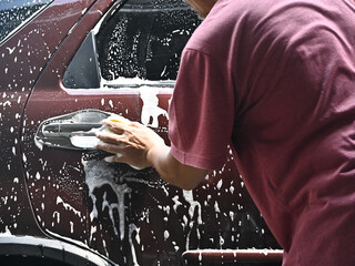 Photo of a man wearing a t-shirt washing or cleaning his car alone. Washing the car with soap and water during the day.