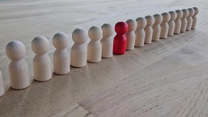 Group of wooden figures lined up with one red figure standing out in a row on a wooden floor at a workshop