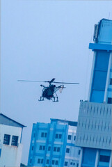 Silhouette helicopter is flying on isolated blue sky in a city