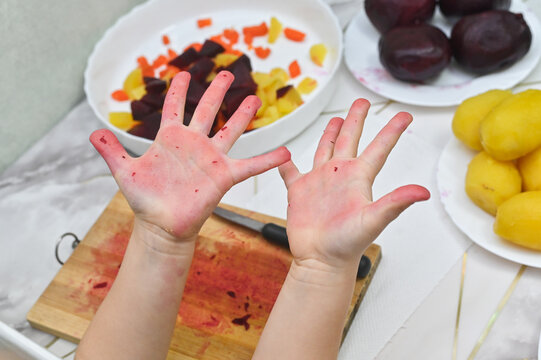 child shows his hands in the kitchen, stained with beets and carrots. The little girl's hands are red from vegetables. The child cooks in the kitchen, her palms smeared.