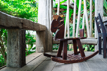 Vintage wooden rocking horse on rustic wooden terrace with tropical greenery, traditional childhood toys, natural lifestyle, countryside home decor and nostalgic outdoor play environment.