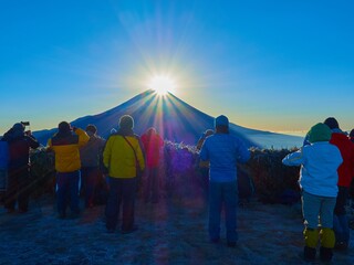 冬の朝の山梨県富士河口湖町 竜ヶ岳山頂からダイヤモンド富士を眺める登山者
