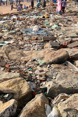 Plastic trash and debris pile up on rocks near the beach, showing coastal pollution and marine litter problem along the shoreline.
