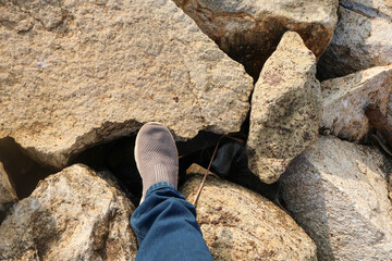 Person walks carefully on large coastal boulders of the Shangumugham Beach sea wall, wearing casual shoes and jeans in warm evening light.