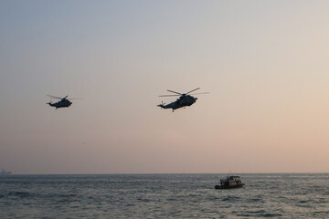 Trivandrum India December 3 2025 : Indian Navy helicopters skim low over the Arabian Sea near Shangumugham Beach during Navy Day demo as a patrol boat tracks their sunset flight.