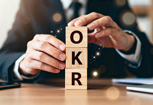 Businessperson carefully stacking wooden blocks to form okr acronym, symbolizing business objectives key results framework success
