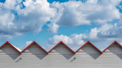 Sawtooth Roof Line with Red Gable Edges Against Blue Sky and Clouds